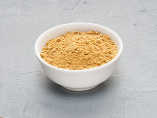 Spice dry ginger in white ceramic cup on gray concrete background. Indian cuisine, ayurveda, naturopathy concept