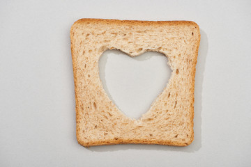Top view of bread slice with carved heart shape on grey background