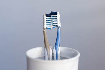 Two plastic toothbrushes kissing in toothbrush cup on grey background representing a couple in love. Dental care, romantic relations and love concept