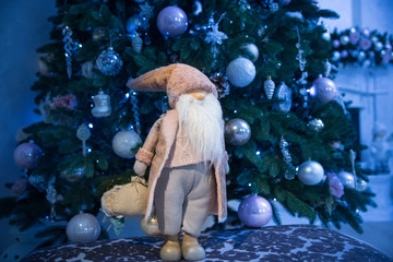 A Christmas toy stands on a chair near a Christmas tree which is decorated with glass balls, cones...