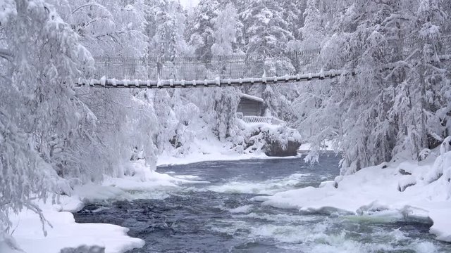 a person walking on suspension bridge crossing river rapids at winter
