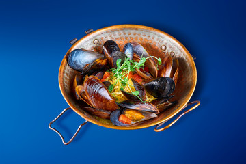 Close up view on tasty Bowl with mussels in shells isolated on blue. Delicious seafood appetizer