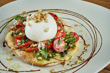 Close up view on Italian burrata cheese with focaccio sauce, tomatoes, basil and nuts. Restaurant dish on a wooden background. Close up view. Food flat lay