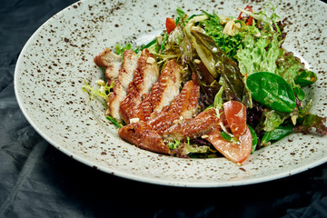 Salad with spinach, lettuce, olive oil, smoked eel in a stylish white ceramic plate on a black background. Healthy and diet food. Seafood salad