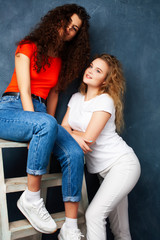 young pretty teenage girls friends with blond and brunette curly hair posing cheerful on blue background, lifestyle people concept