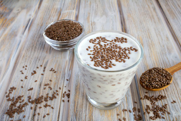 Yogurt or kefir with flax seeds in the glass on the light brown wooden  background. Closeup.