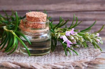 Rosemary essential oil in a glass bottle with fresh green rosemary herb on old wooden table for spa, aromatherapy and bodycare.Selective soft focus.Copy space.