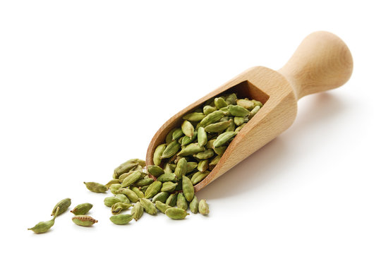 Green cardamom pods in wooden scoop.
