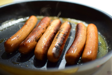Fried sausages at the time of cooking in a pan. The effect of haze due to hot steam.