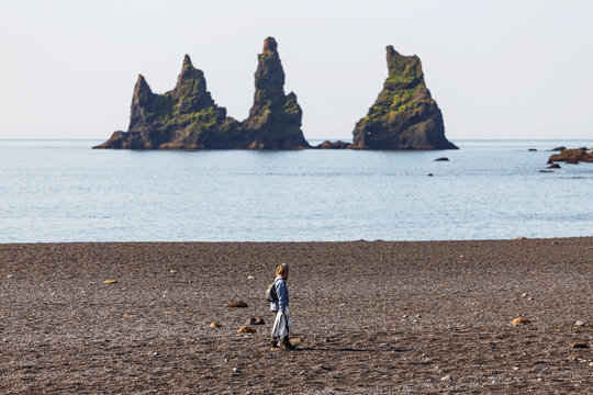 Woman Walking Along the Beach Looking at the Prominent Sea Stacks in Vik, Iceland - Powered by Adobe