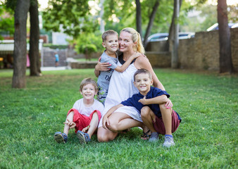 Young woman and three young boys in summer park. Mother and children outdoors.