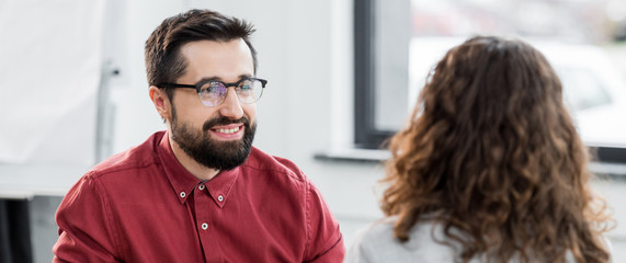 panoramic shot of smiling account manager looking at colleague