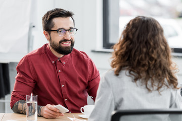 selective focus of smiling account manager looking at colleague