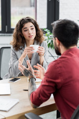 selective focus of account manager holding cup and listening to colleague