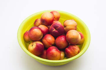 Ripe peaches in a green basket on a white