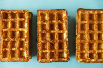 Three belgian waffles on trendy blue background. Minimal food and bakery concept, modern and contemporary style, top view and close up
