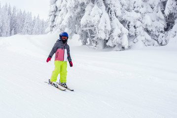 Fototapeta na wymiar Child in ski suit skiing downhill in mountains during winter season