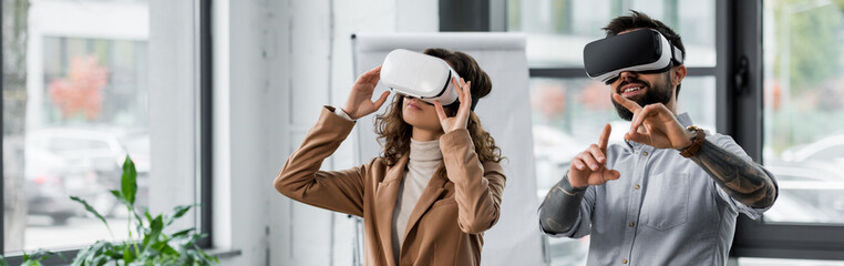 panoramic shot of smiling virtual reality architects in virtual reality headsets pointing with...