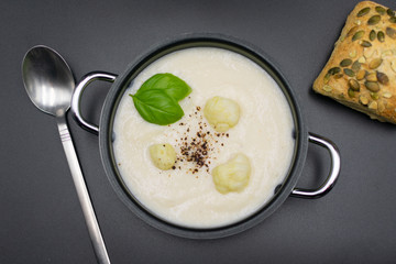 Cauliflower soup in pot with bun on black background. View from above