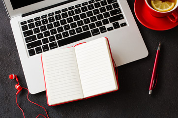 Blank red notebook, computer laptop, headphones and cup of tea.