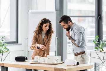 virtual reality architect pointing with finger at model of house and talking with colleague