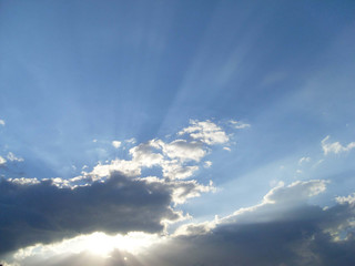 Fototapeta na wymiar Sonnenstrahlen hinter grauen Wolken am blauen Himmel / Blue sky with sun behind clouds