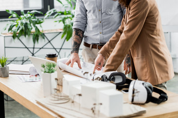 cropped view of virtual reality architects looking and pointing with finger at blueprint