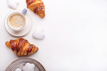 Croissants, glazed cookies and a cup of coffee on a white wooden table. Morning still life. Top...