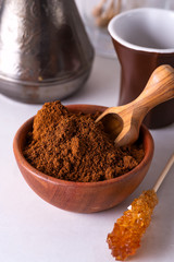 Grinded coffee in a wooden bowl with brown sugar stick on the background of a copper turks