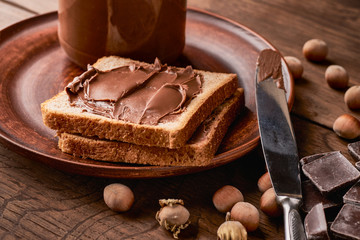 Chocolate nut pasta with slices of toast bread in a plate on a wooden background