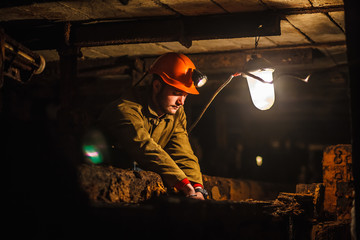 A tired miner in a coal mine looks at the light. Work in a coal mine. Portrait of a miner. Copy...