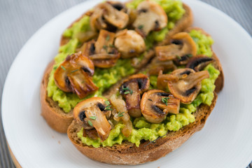 toast with avocado and grilled champignons on the dish close-up