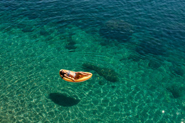 Fototapeta na wymiar Slim young woman in bikini and sunglasses on the air mattress floats in the open sea.