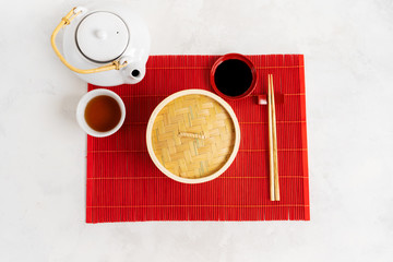 Asian tea food background. Teapot and Cup with chopsticks on the red bamboo mat over the gray stone background with copy space. Mockup for the menu.