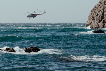 Helicopter with lifeguards flies in stormy weather over sea with strong wind and waves. Search and Rescue operation. Ocean coast with cliffs and rock