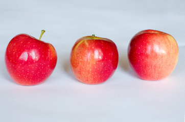 Three fresh red apples lie in a row on a white background. Selective focus. Close up.