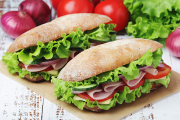 Two sandwiches with fresh vegetables, ham and cheese in ciabatta bread	