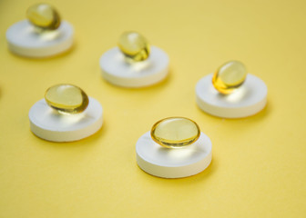 Close-up of golden colored oil supplements, soft gel capsule on top of round white pills, health concept, pharmaceutical tablets