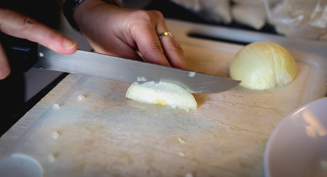 woman cuts onions on a white plastic board