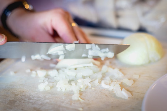 woman cuts onions on a white plastic board