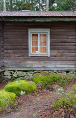 Window of an ancient authentic wooden house of the 17th century near large stones in a forest on the island of Seurasaari in Helsinki, Finland, a cloudy day in late autumn. The harsh beauty of ancient