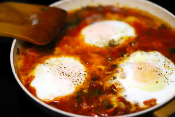 Selective focus. Shakshuka cooked on a frying pan. Cooking Israeli Shakshuka fried eggs. Middle Eastern cuisine. Fried eggs in tomato sauce.