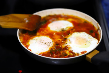Selective focus. Shakshuka cooked on a frying pan. Cooking Israeli Shakshuka fried eggs. Middle Eastern cuisine. Fried eggs in tomato sauce.
