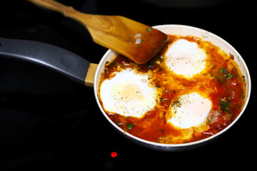 Selective focus. Shakshuka cooked on a frying pan. Cooking Israeli Shakshuka fried eggs. Middle Eastern cuisine. Fried eggs in tomato sauce.