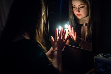 A girl in a dark room, divines with candles in her hand in front of a mirror, looks in her reflection and sees her future.