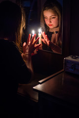 A girl in a dark room, divines with candles in her hand in front of a mirror, looks in her...