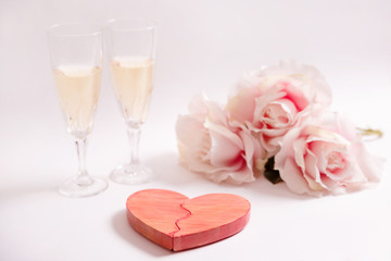 San Valentín. Corazón rojo de madera, dos copas de vino blanco y rosas sobre fondo blanco.