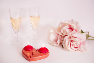 San Valentín. Corazón rojo de madera con velas, dos copas de vino blanco y rosas sobre fondo blanco.