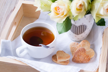 Cup of tea, wooden heart and bouquet of roses in tray