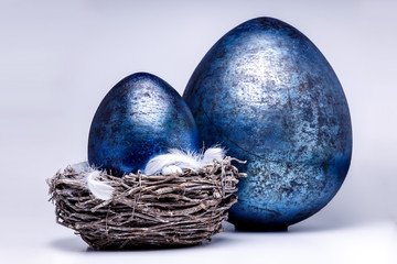Zwei blaue Eier, eines davon in einem Osternest mit weißen Federn zum Ostertag